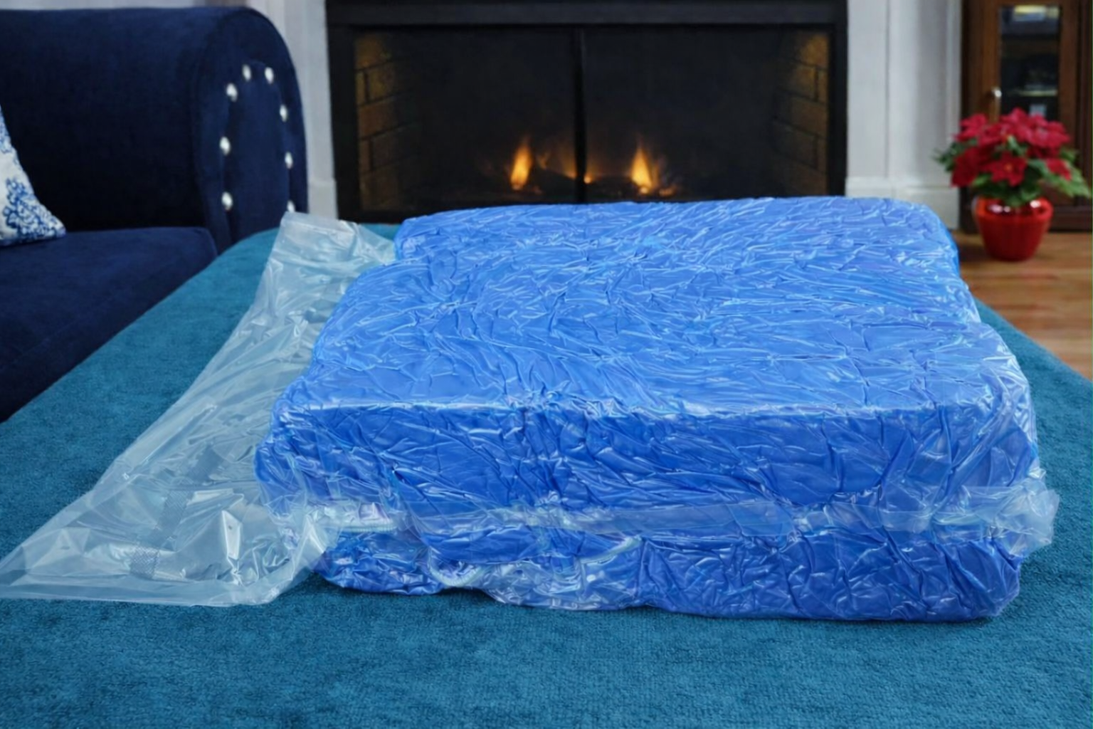 Blue HerPillow mens body pillow covered vacuum-sealed on a blue couch in a room with a fireplace.
