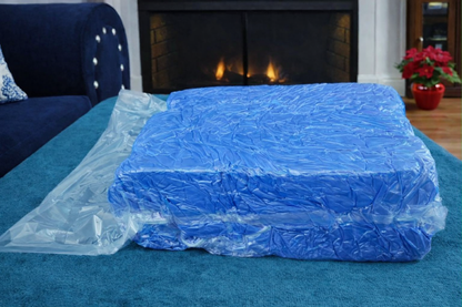 Blue HerPillow mens body pillow covered vacuum-sealed on a blue couch in a room with a fireplace.