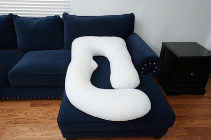 White U-shaped pillow on a dark blue sofa with a neutral background