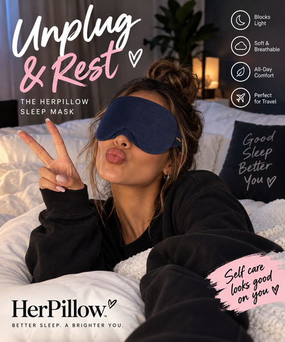A woman wearing a navy blue HerPillow sleep mask lies in bed, making a peace sign and puckering her lips. The image features promotional text overlays for 'Unplug & Rest' and highlights the product's benefits like blocking lights, being soft and breathable, and being comfortable all day.