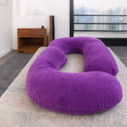 Herpillow Purple U-shaped pillow on a rug in a room with a wooden side table and large window.