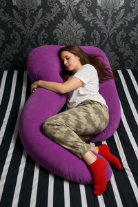 Woman resting on her side with a purple HerPillow full body pillow, showing a cozy everyday use position.